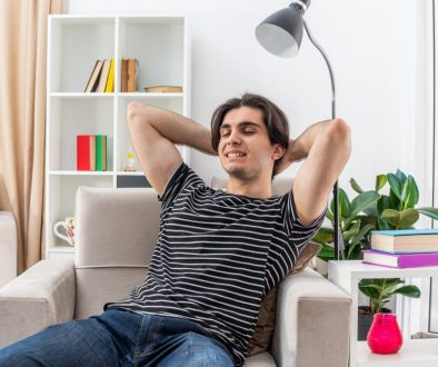 young man in casual clothes happy and positive relaxing spending weekend sitting on the chair in light living room